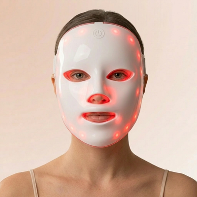 Kvinne med InfraRelief™ LED-ansiktsmaske i hvitt med rødt lys, forfra mot beige bakgrunn