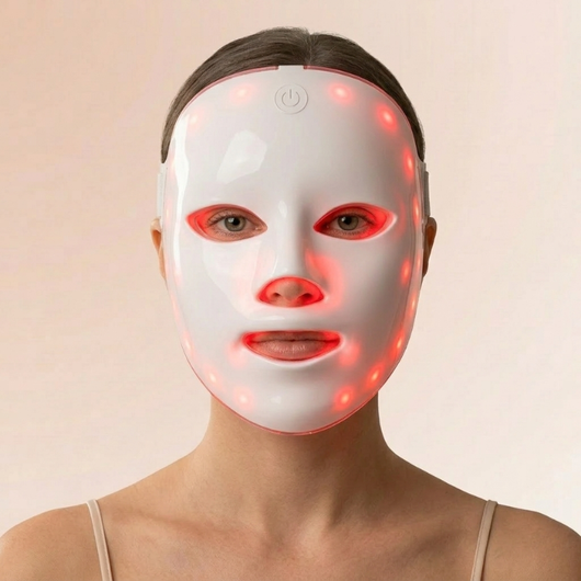 Kvinne med InfraRelief™ LED-ansiktsmaske i hvitt med rødt lys, forfra mot beige bakgrunn