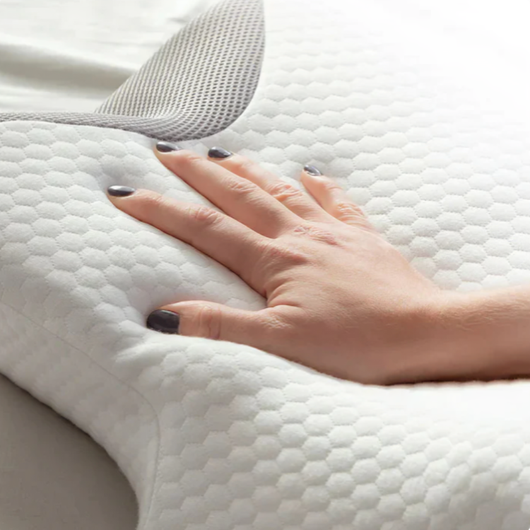 Nærbilde av hånd som trykker på ergonomisk minneskumspute med hvit honeycomb-trekk