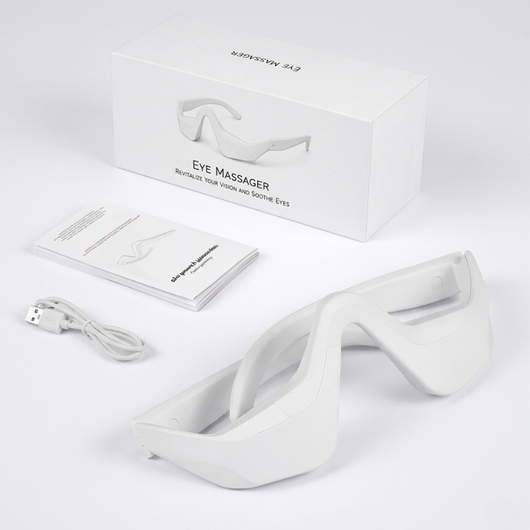InfraRelief™ øyemassasjeapparat – hvit enhet, USB-ladekabel, brukerhåndbok og emballasje mot hvit bakgrunn