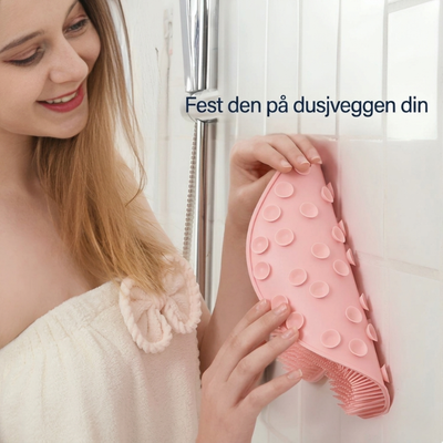En kvinne fester en rosa skrubbematte på dusjveggen med sugekopper; teksten på bildet lyder: «Fest den på dusjveggen din»