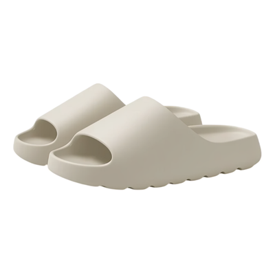 Slip-on-tøfler i beige EVA-materiale med tykk, myk såle og bølgemønstret underside, mot hvit bakgrunn