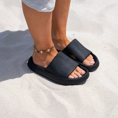 Person med svarte ergonomiske tøfler på sand – støtdempende sommertøfler med sklisikker såle for bruk på stranden og utendørs